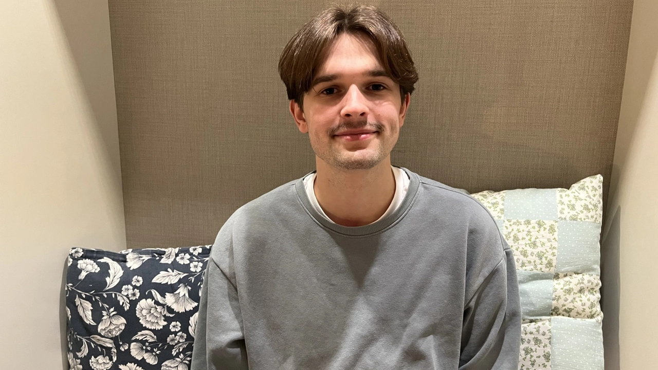 Porträttbild på Joakim Wiksten, beige vägg och mönstrade kuddar i bakgrunden