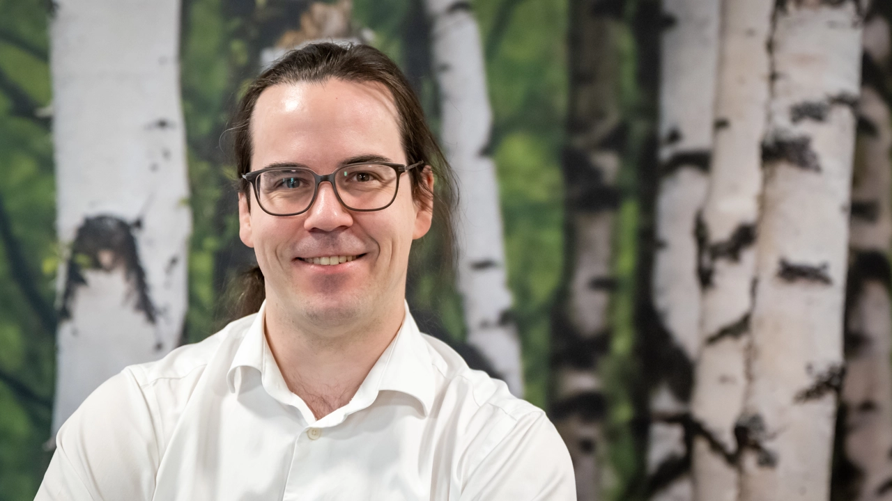 En man med glasögon sitter framför en målning