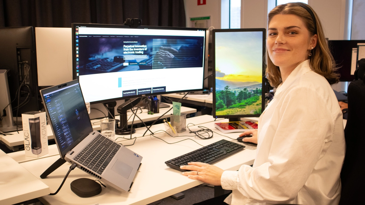 Bild på Johanna Petersson sittande vid skrivbord med flera datorskärmar omkring sig.