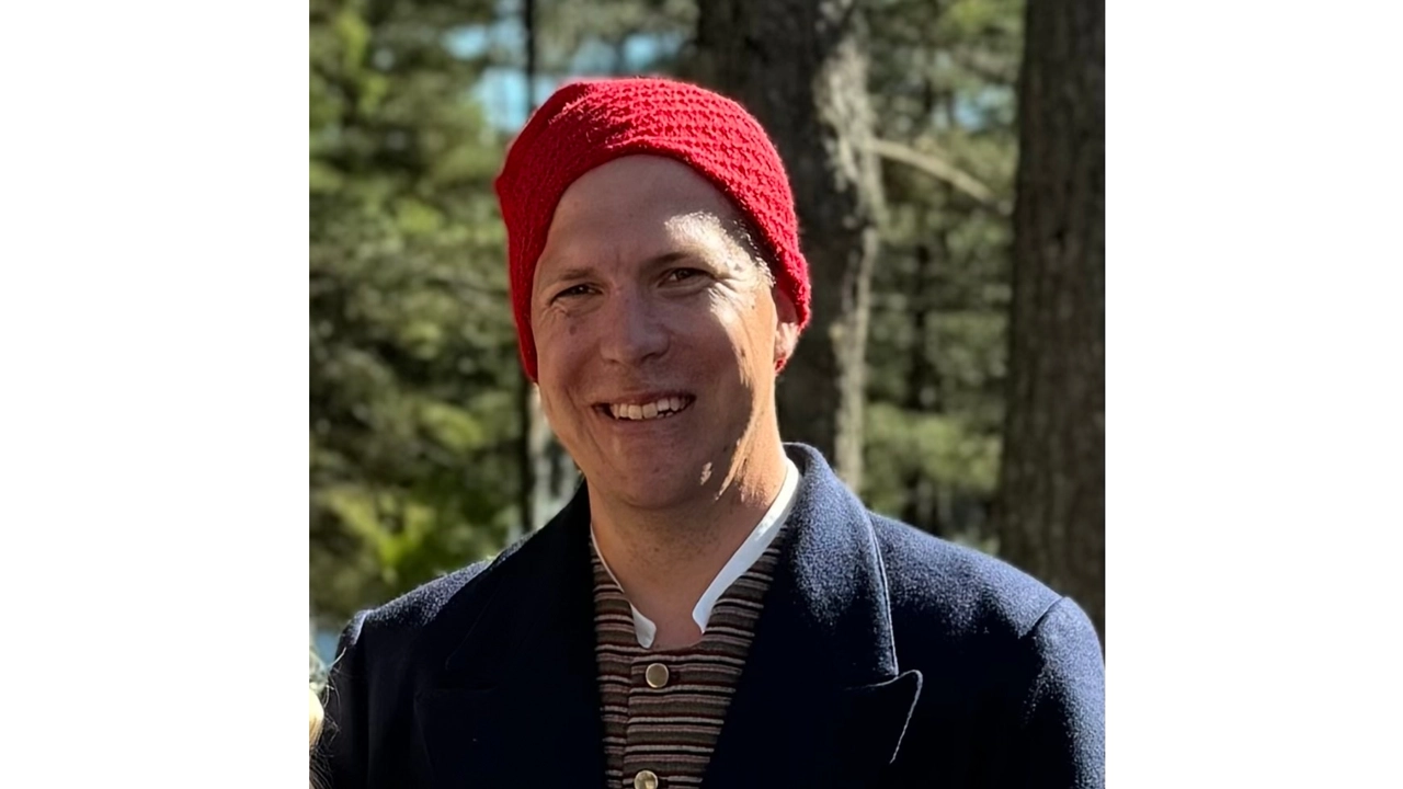 Jon Månsson med en röd mössa och en skog i bakgrunden. 