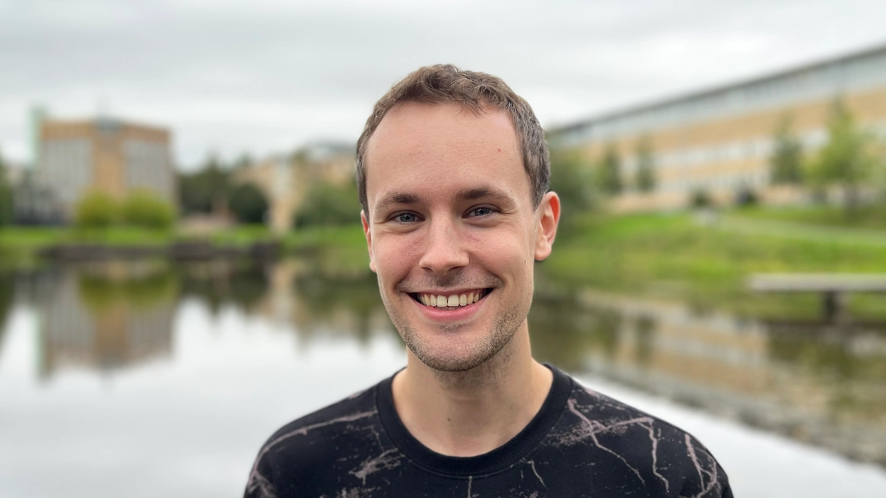 A male student with a broad smile in front of the Campus Pond. 