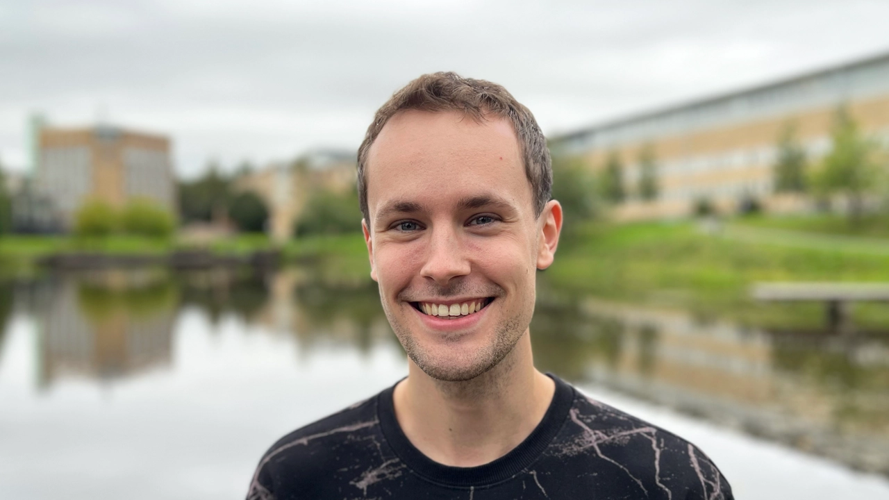 A male student with a broad smile in front of the Campus Pond. 