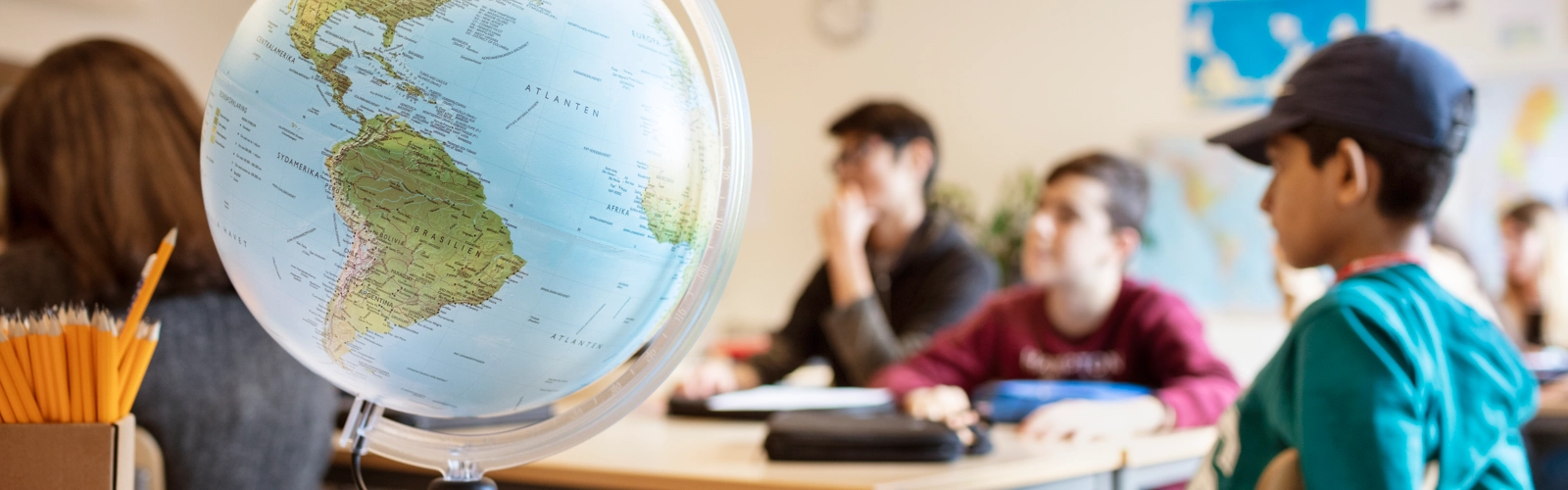 En ung pojke sitter vid ett skrivbord med en jordglob på.