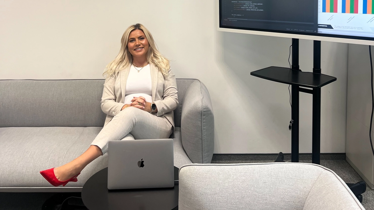 Bild på Julia Larsson sittande i en soffa, företagslogga på väggen bakom henne.