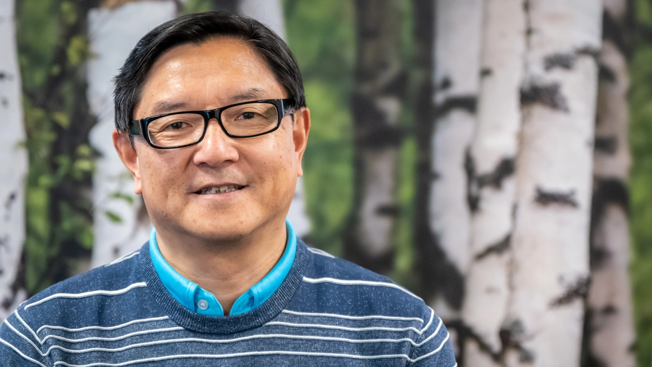 En man i glasögon som står framför en målning av träd