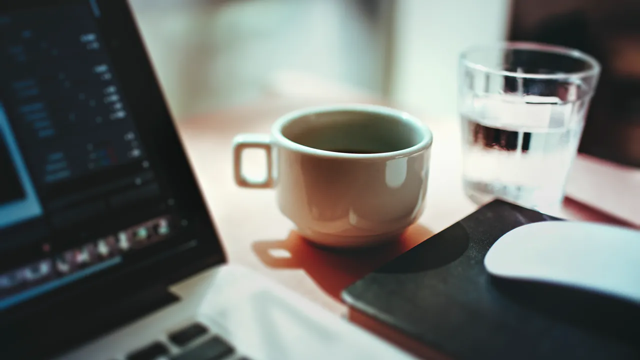 A picture of a coffee cup, a glass of water and a laptop.