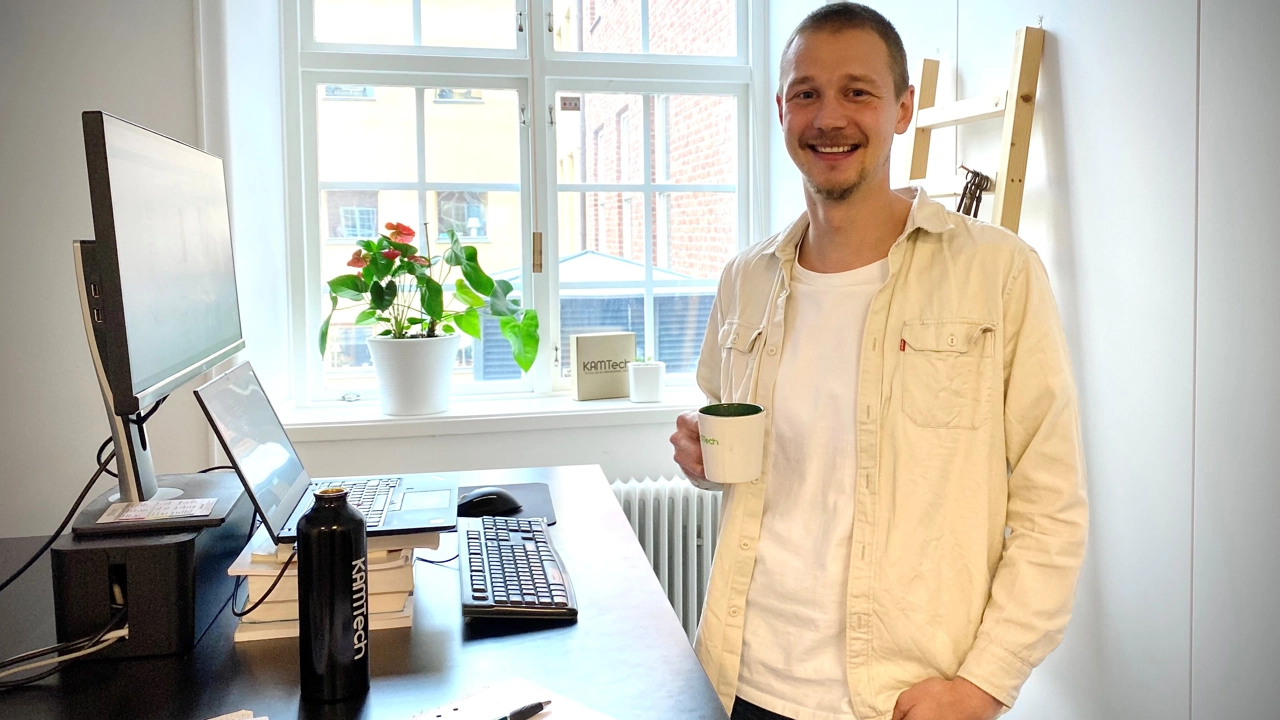 Bild på Kalle Almstedt stående i sitt arbetsrum med kaffemugg i handen