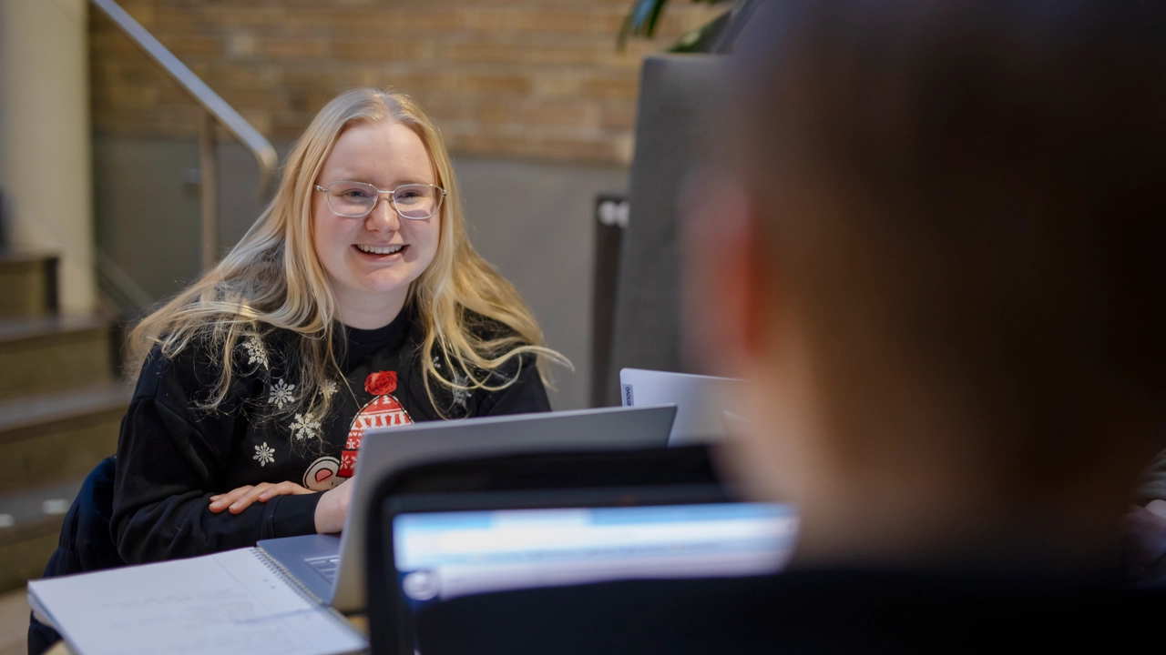 En leende student i samtal med en annan vid en av universitetets tillgängliga studieplatser. 