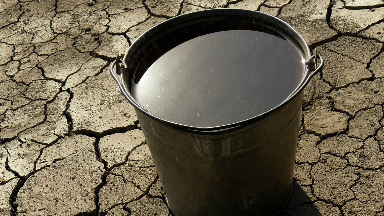 Hink med vatten på söndertorkad mark som illustration av klimatförändringarna.