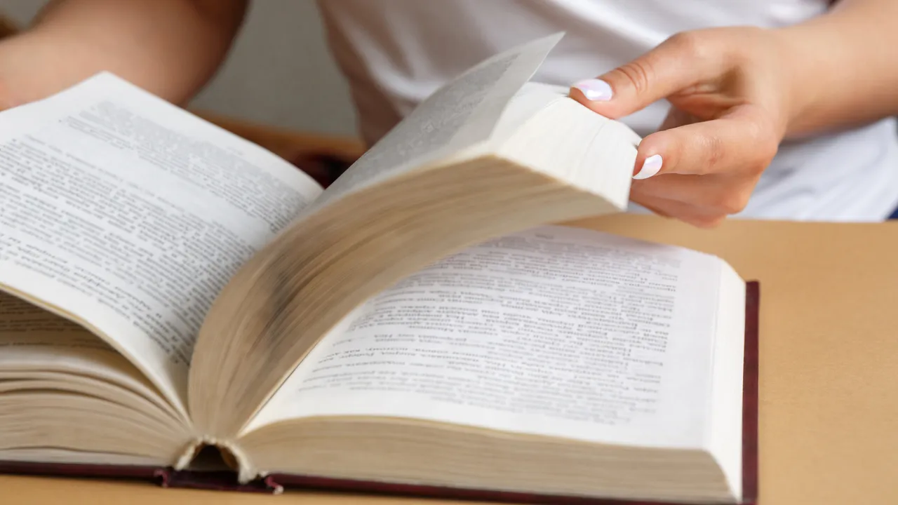 Närbild på händer som bläddrar i en bok.