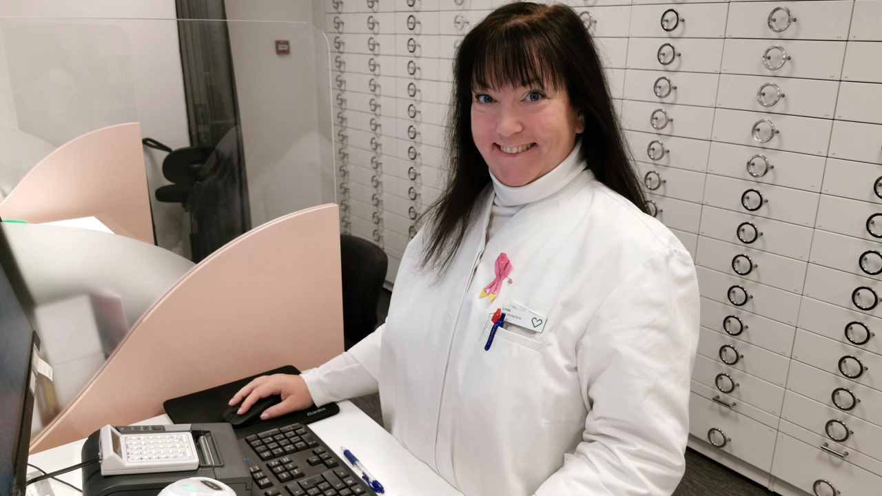 Bild på receptarien Lindha Lydahl i vit rock bakom disken på ett apotek