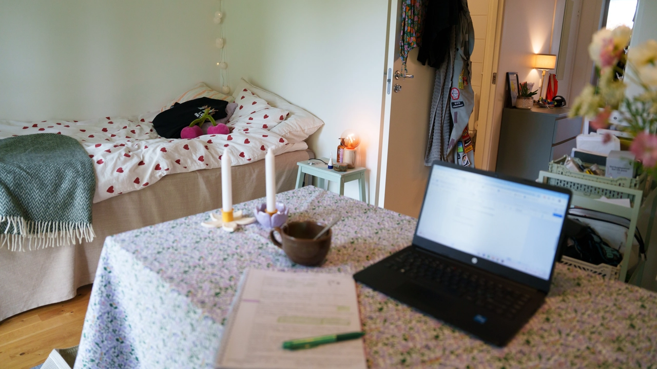 Bild på en dator på ett köksbord och en säng i bakgrunden. 