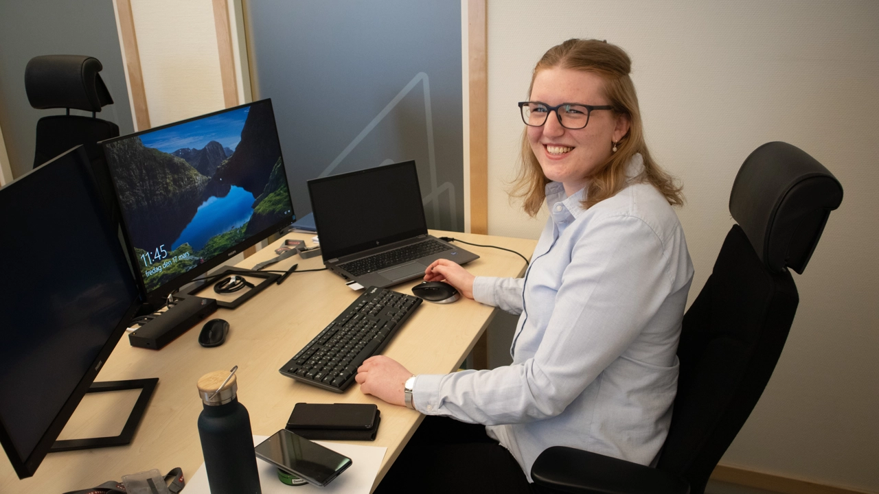 Bild på Linnea Stålstam sittande vid skrivbord med flera datorskärmar framför sig