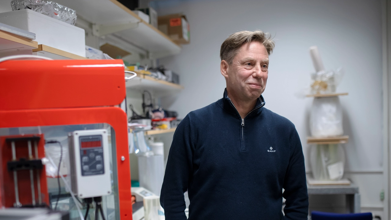 En man står i en labbmiljö med utrustning runtom sig.