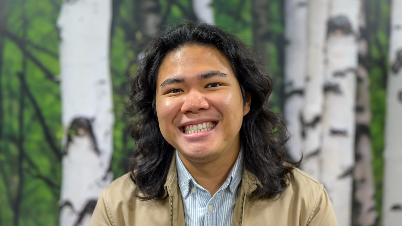 A man smiling in front of a painting of birch trees.