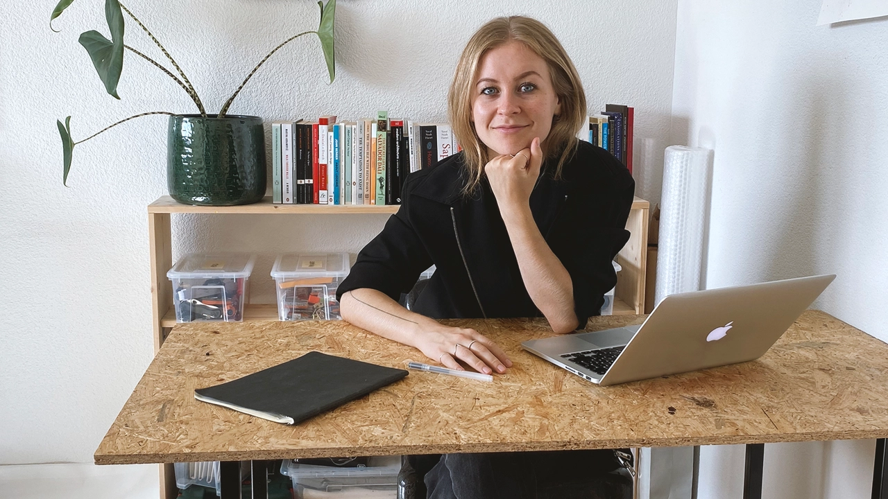 Bild på Maja Malmcrona sittande vid skrivbordet med dator framför sig.