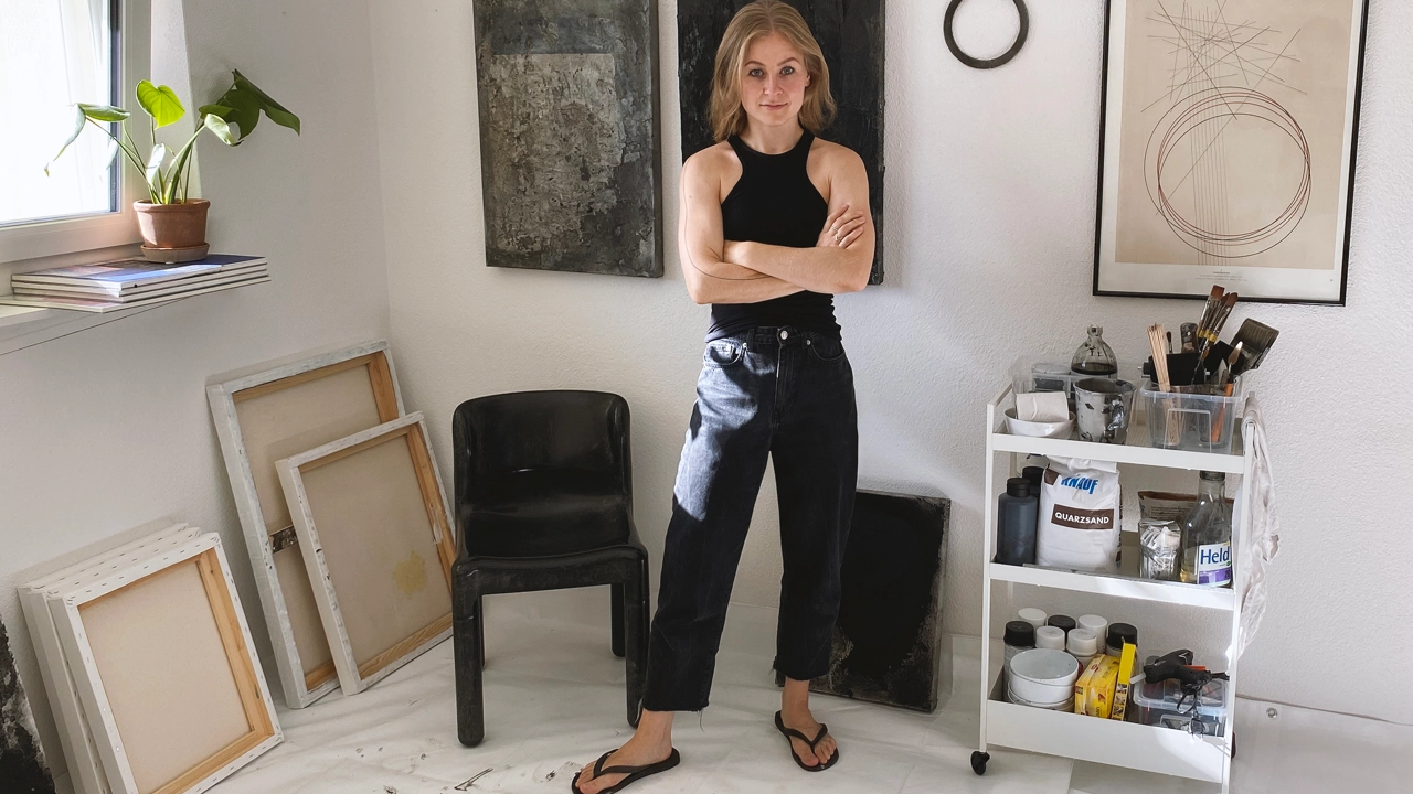 Bild på Maja Malmcrona stående i sitt arbetsrum, skisser på golvet framför henne