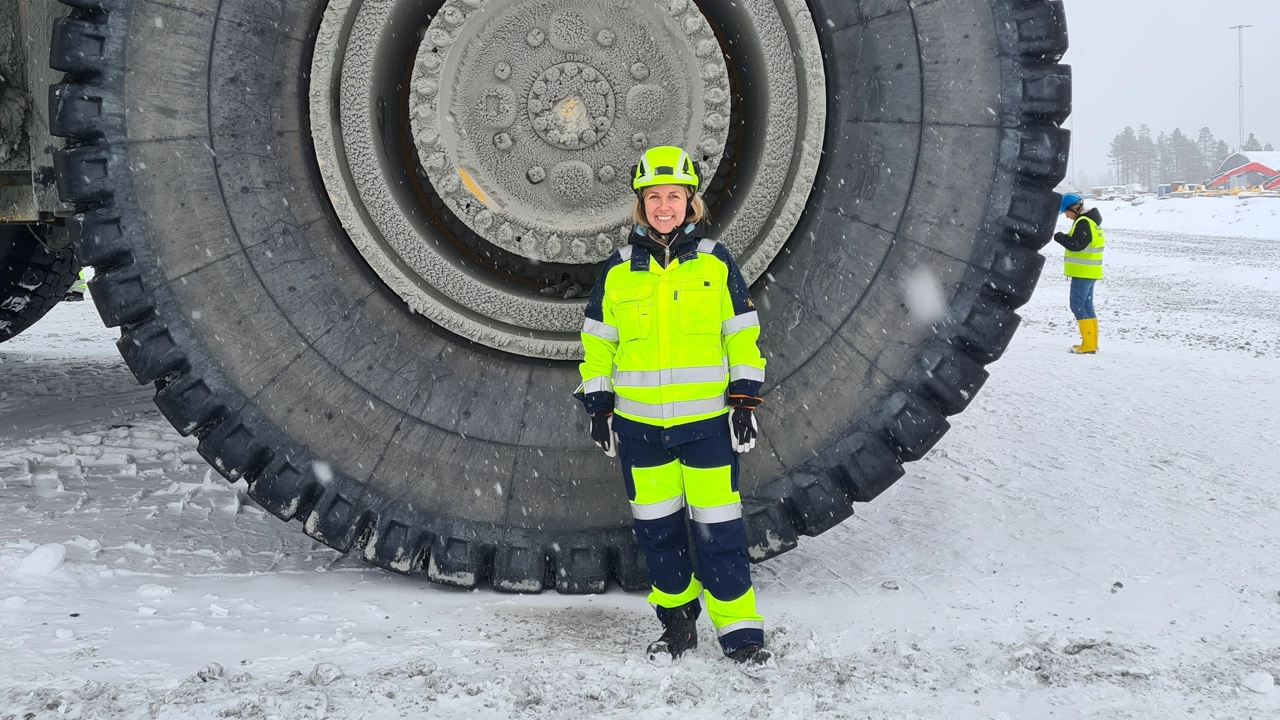 Bild på Malin Suup i reflexkläder och skyddshjälm framför hjulet till en stor gruvmaskin