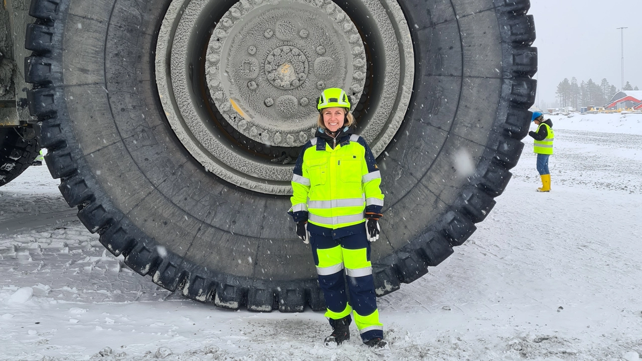 Bild på Malin Suup i reflexkläder och skyddshjälm stående framför hjulet till en stor gruvmaskin