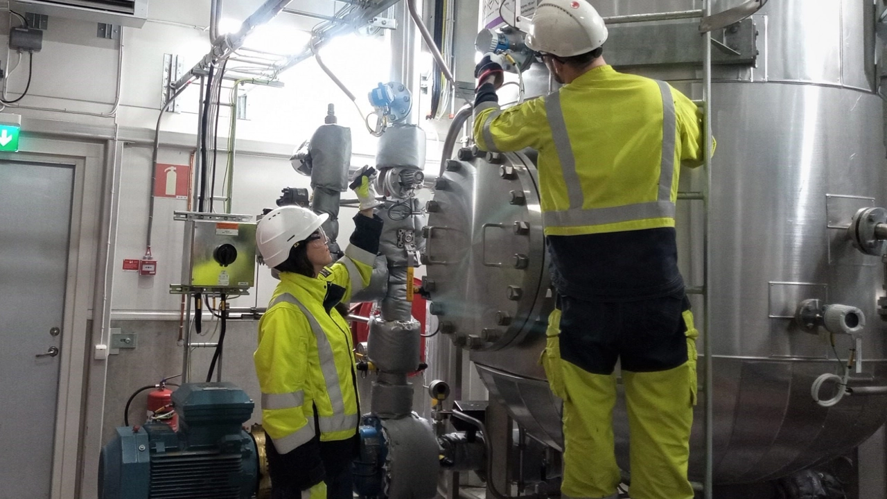 Bild på Maria Teike i hjälm och reflexkläder i fabriken tillsammans med kollega