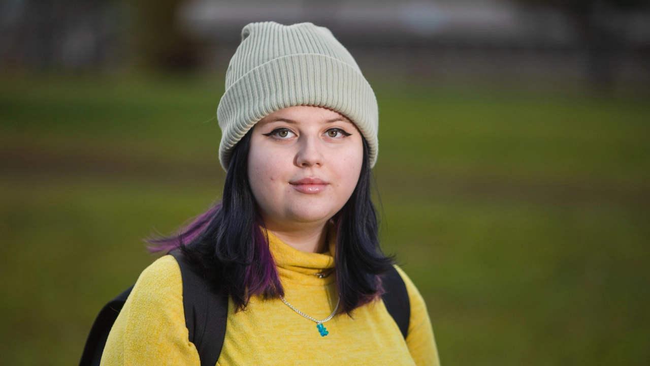 En kvinna med långt svart hår som bär en gul tröja och en mössa.