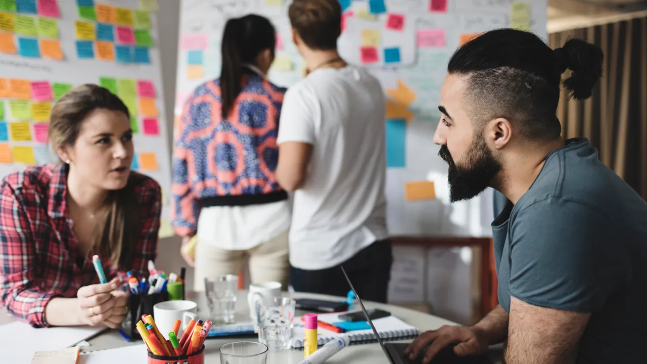 Grupparbete, kvinna och man pratar vid ett bord med pennor och papper.