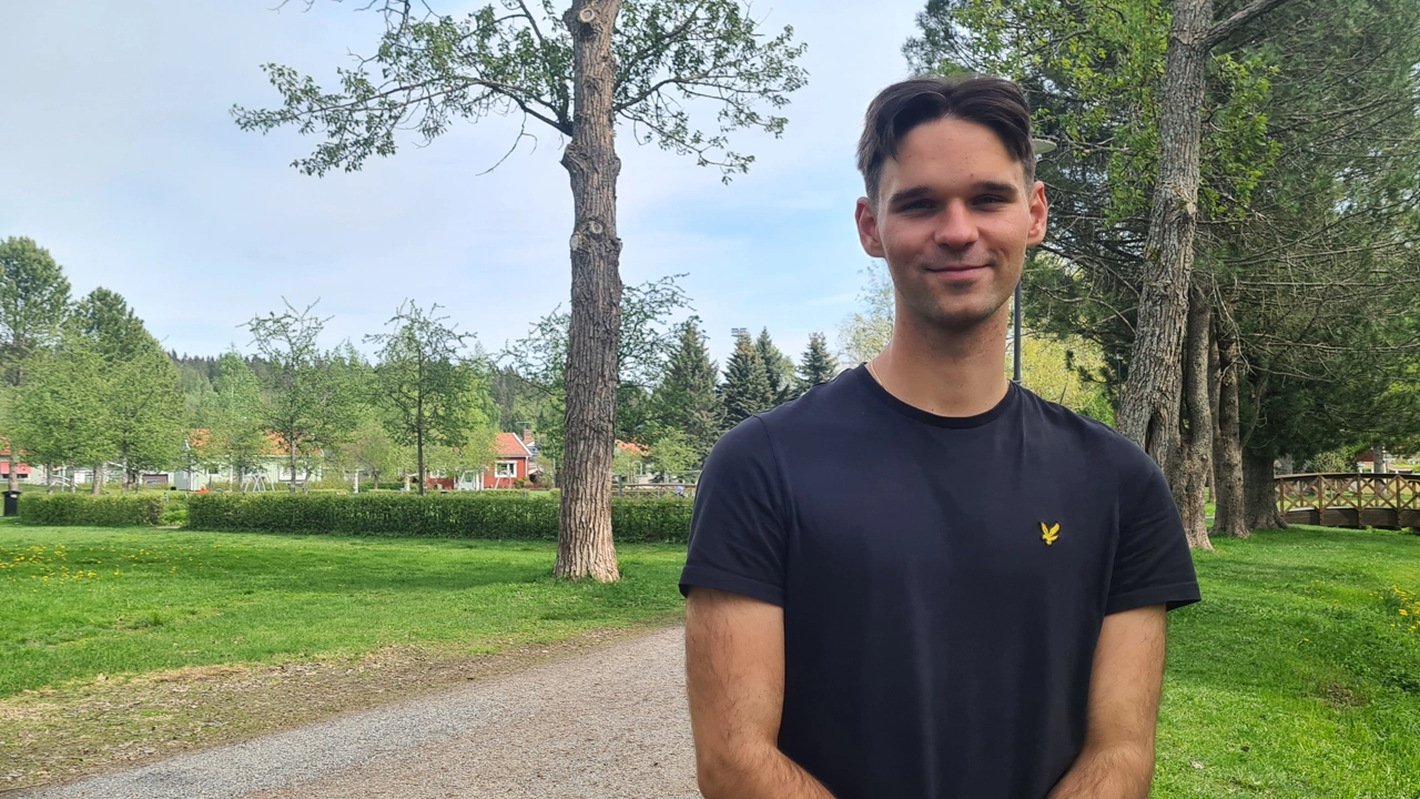 En man står framför ett träd på en grusväg.