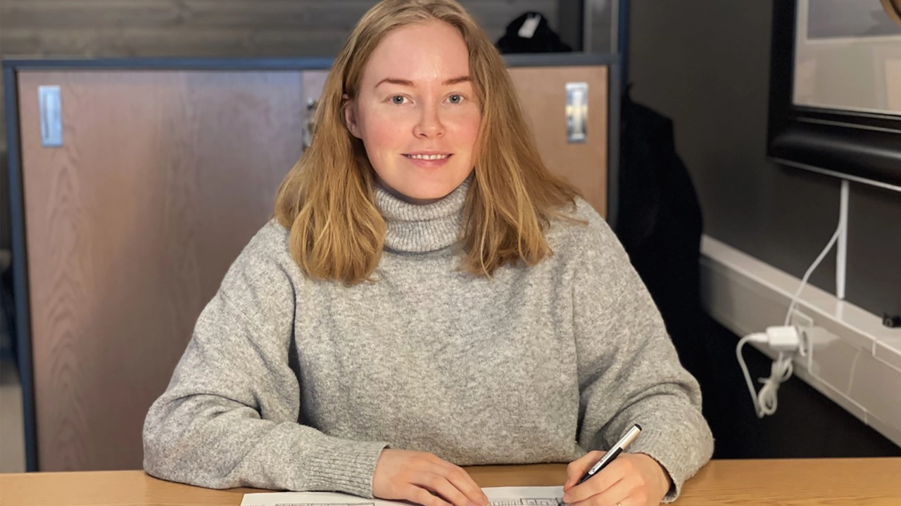 Bild på Minna Portinsson sittande vid ett skrivbord med penna i handen.