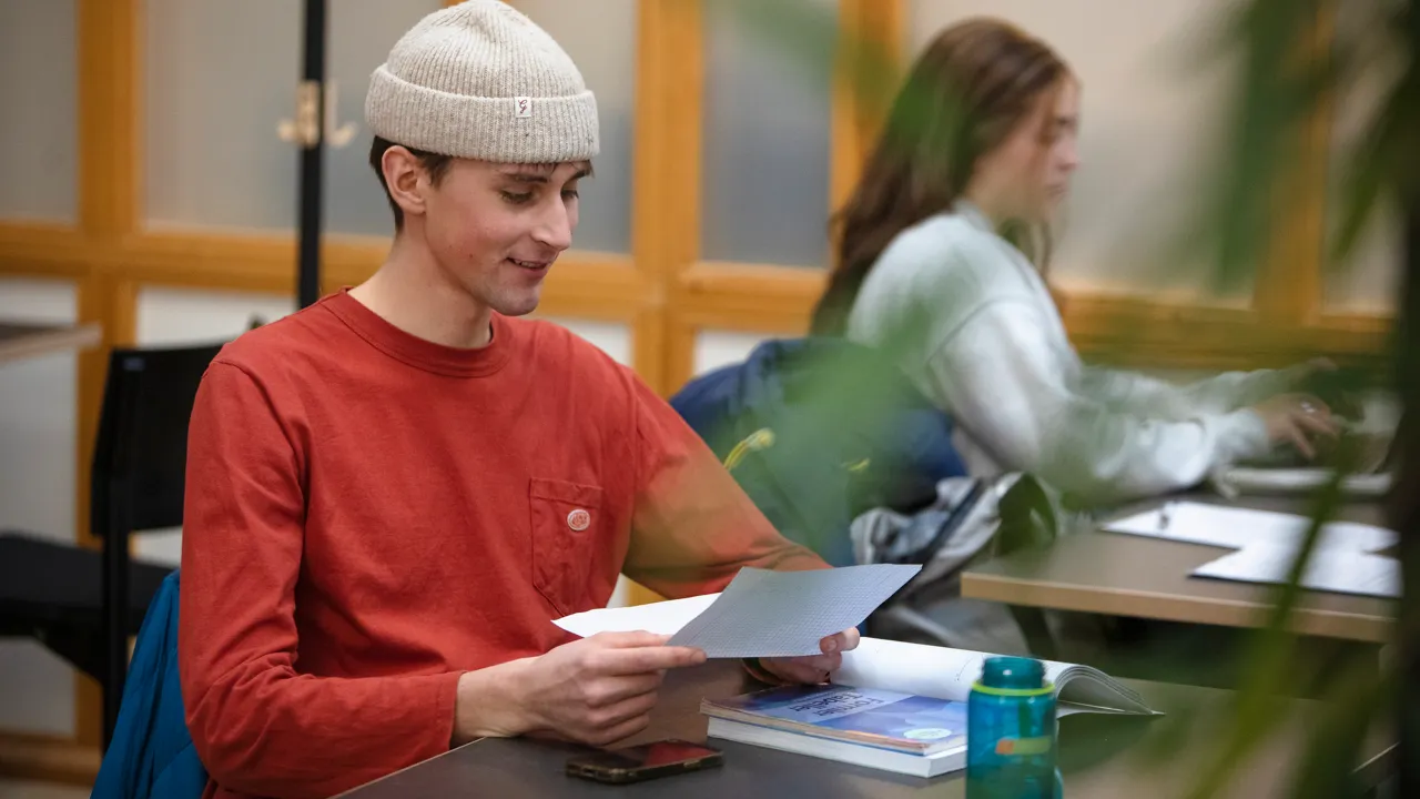 En man sitter med ett papper i handen vid en studieplats.