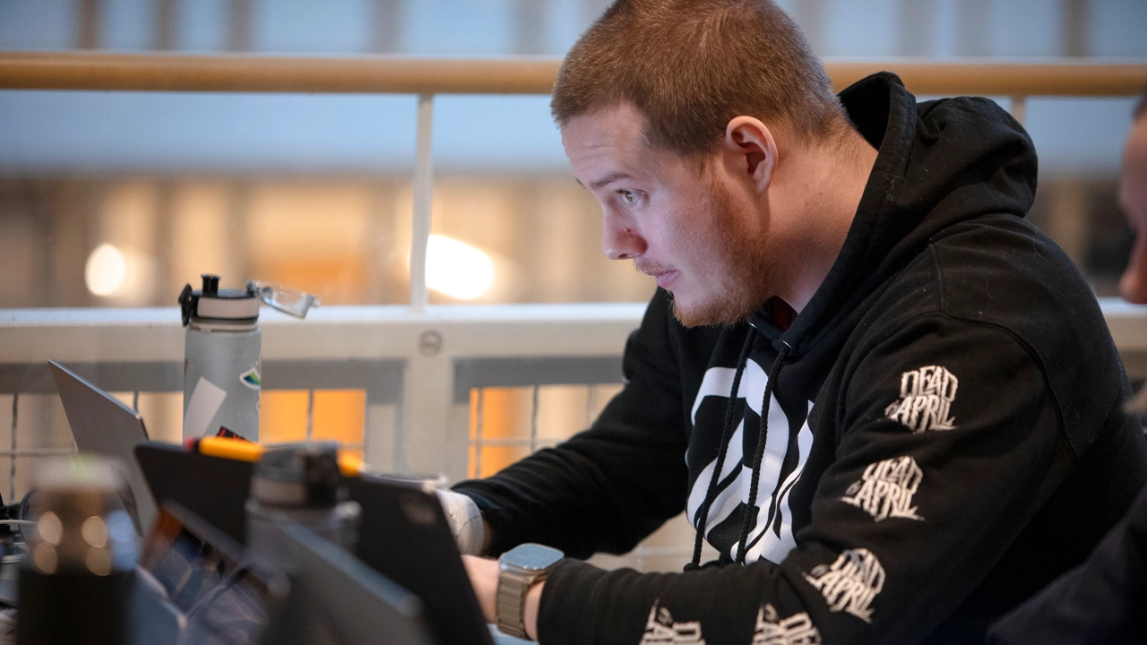 En man sitter vid ett bord och använder en bärbar dator.