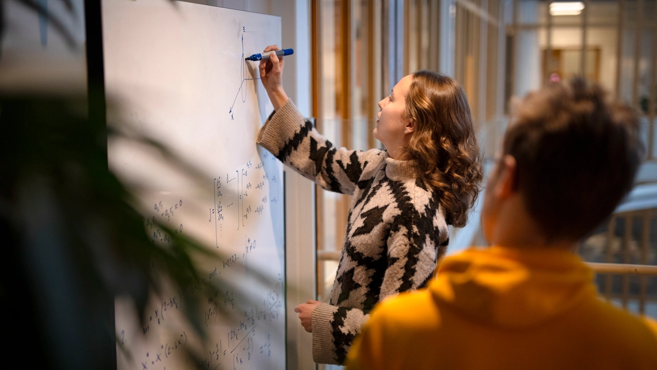 Ett vindkraftverk i centrum med en blå himmel bakom på ovandelen, och en älv på nederdelen. 