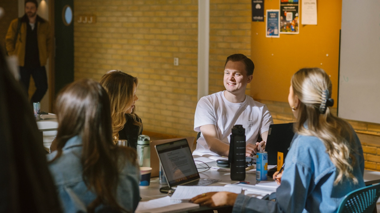 Studenter sitter tillsammans vid ett bord, pratar och pluggar.