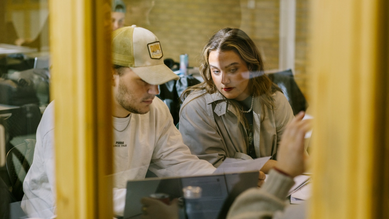 Två djupt koncentrerade studenter skriver på ett arbete tillsammans framför en laptop.