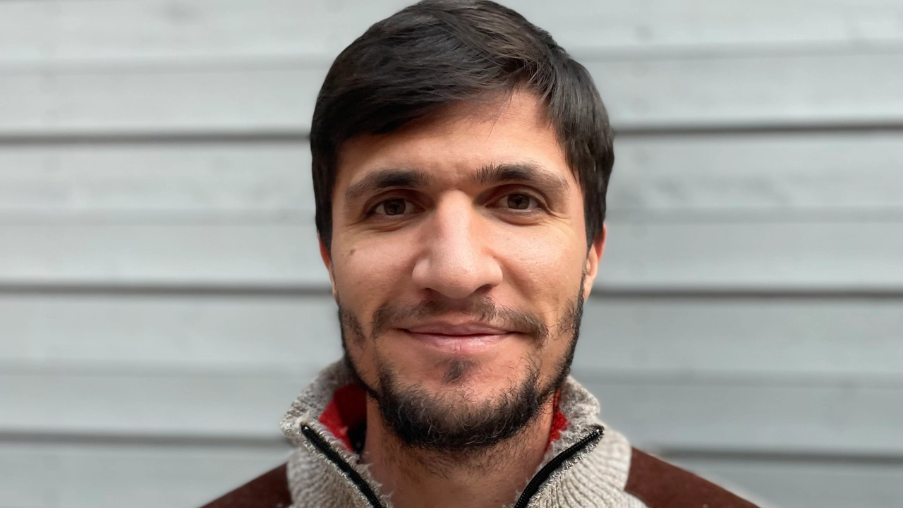 Porträtt på Najmaalddin Saifaddin Dawoud stående mot en väggpanel i grått trä.