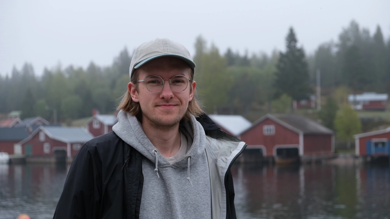 En man med hatt och glasögon står framför ett vattendrag.