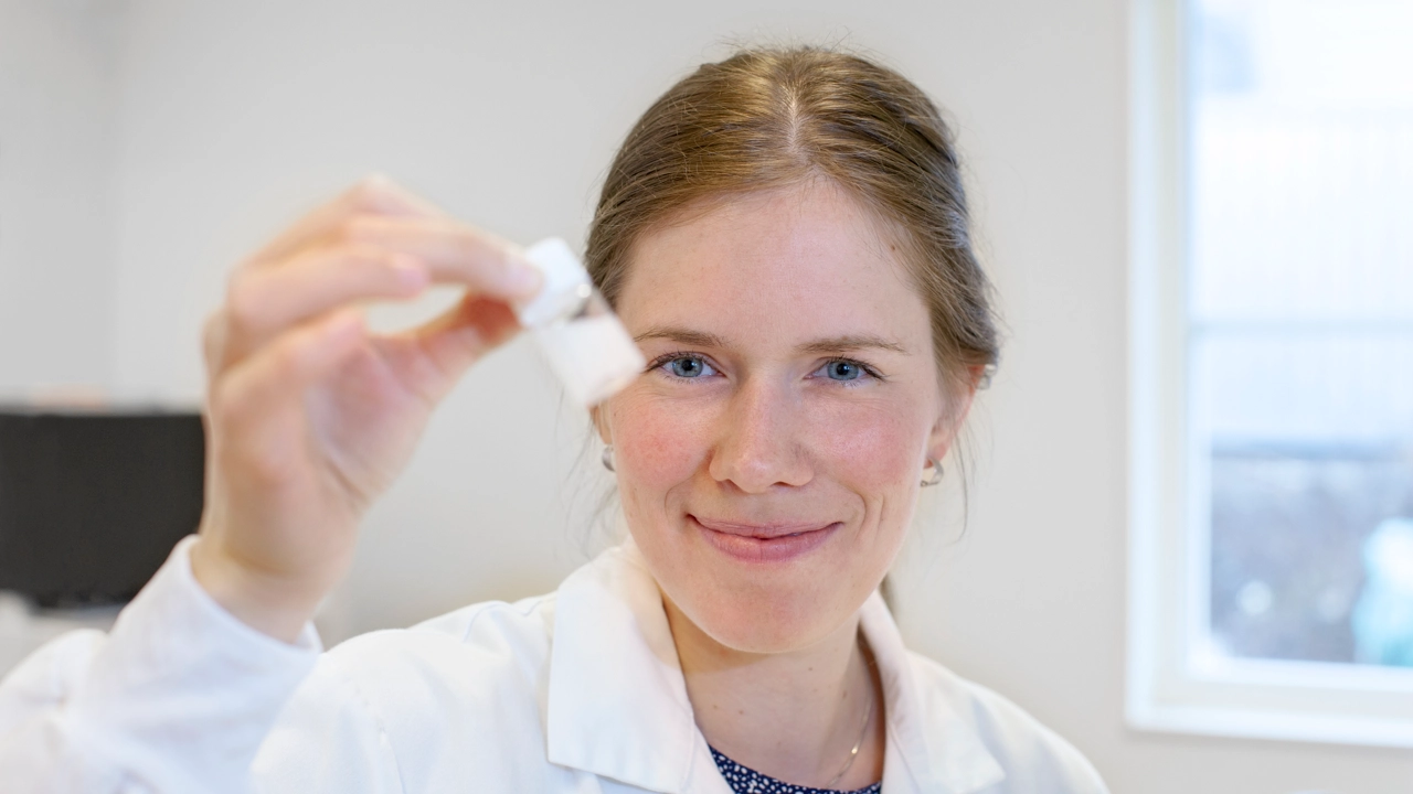 Bild på Nora Ingebrand i laboratoriemiljö, håller upp behållare med vit vätska.