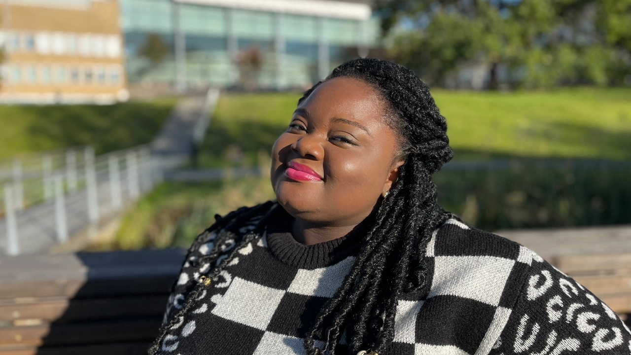 A woman is posing in front of the Campus Pond on a sunny day.