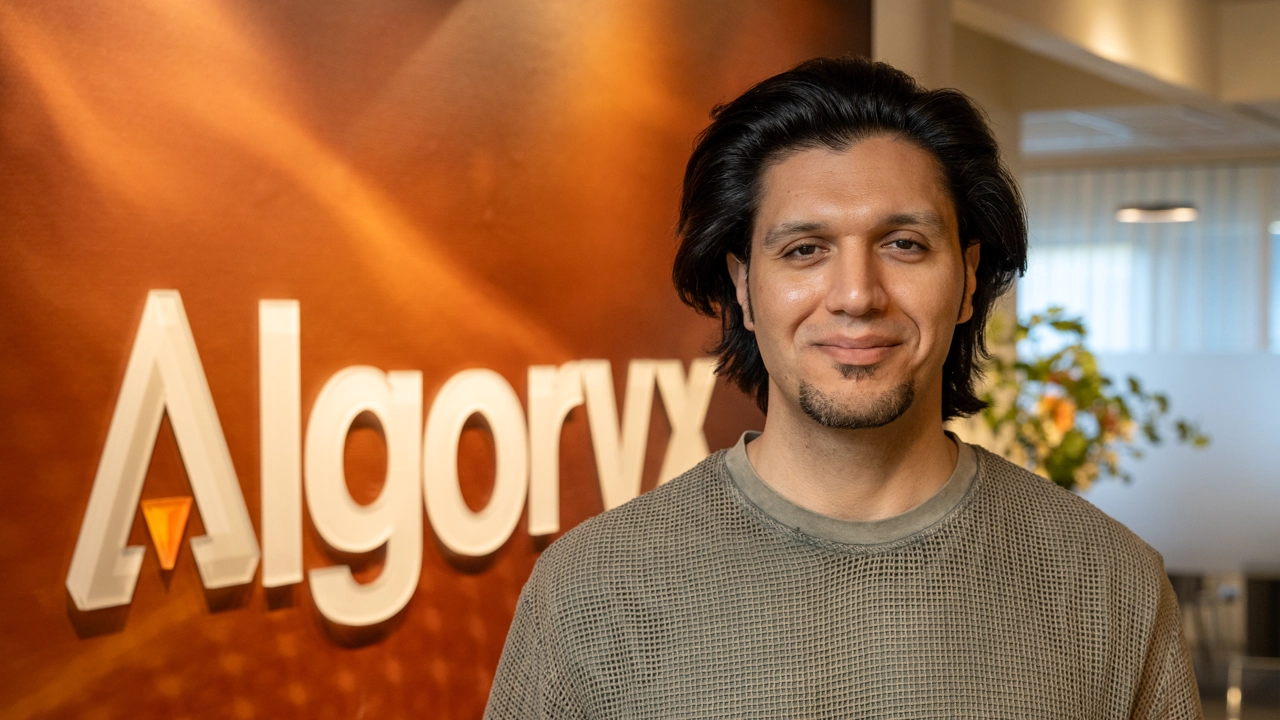 Porträttfoto på Omar Abrahamsson, i bakgrunden Algoryx logotyp mot röd vägg.