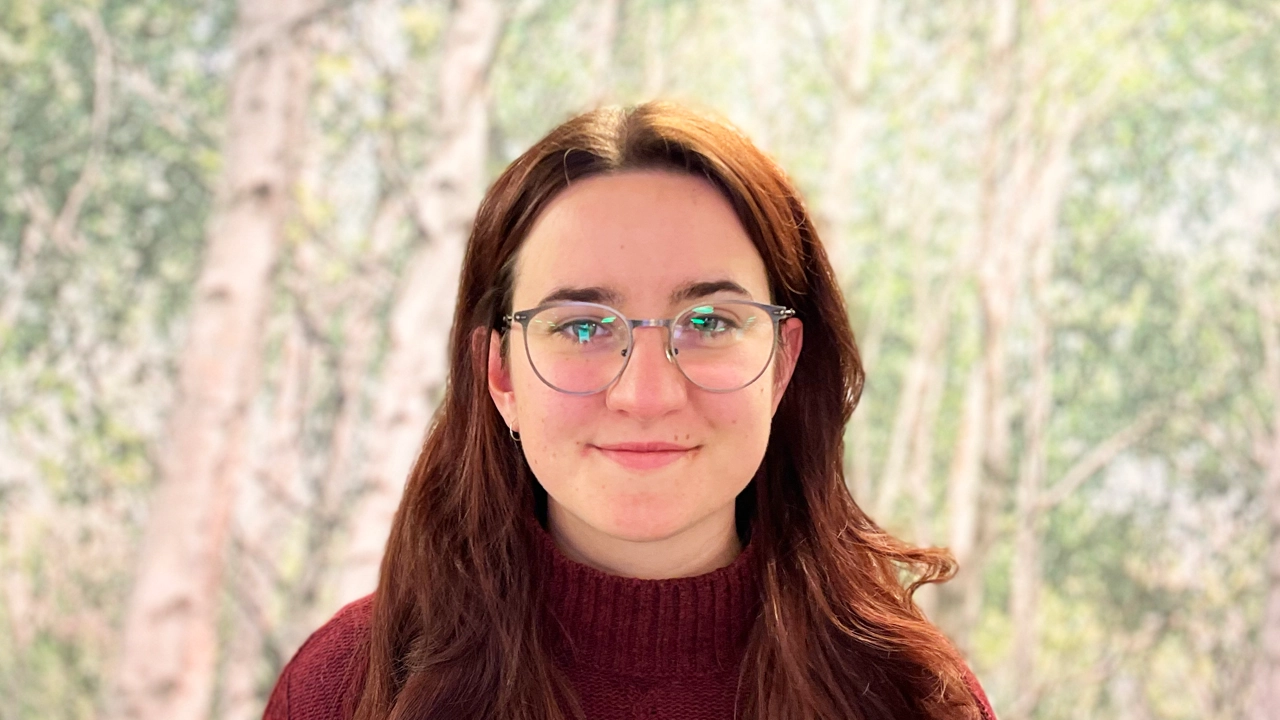Portrait of Polona in front of a picture of birch trees.