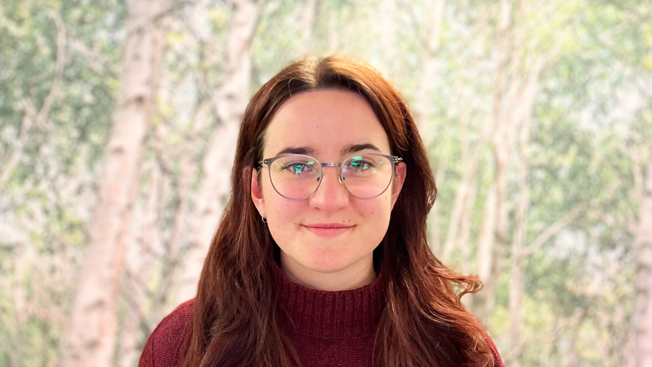 Portrait of Polona in front of a picture of birch trees.