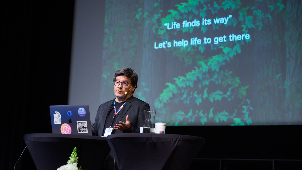 Ricard Solé, public speaker for the 15 year IceLab anniversary public lecture on terraforming ecosystems, seen here against an AI-generated backdrop depicting an arid ecosystem being transformed to a lush one thanks to synthetic organisms.