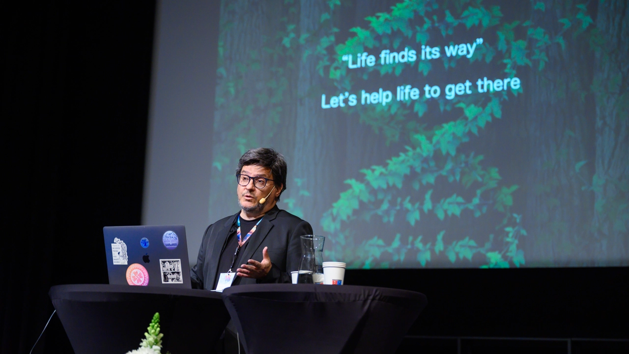 Ricard Solé, public speaker for the 15 year IceLab anniversary public lecture on terraforming ecosystems, seen here against an AI-generated backdrop depicting an arid ecosystem being transformed to a lush one thanks to synthetic organisms.