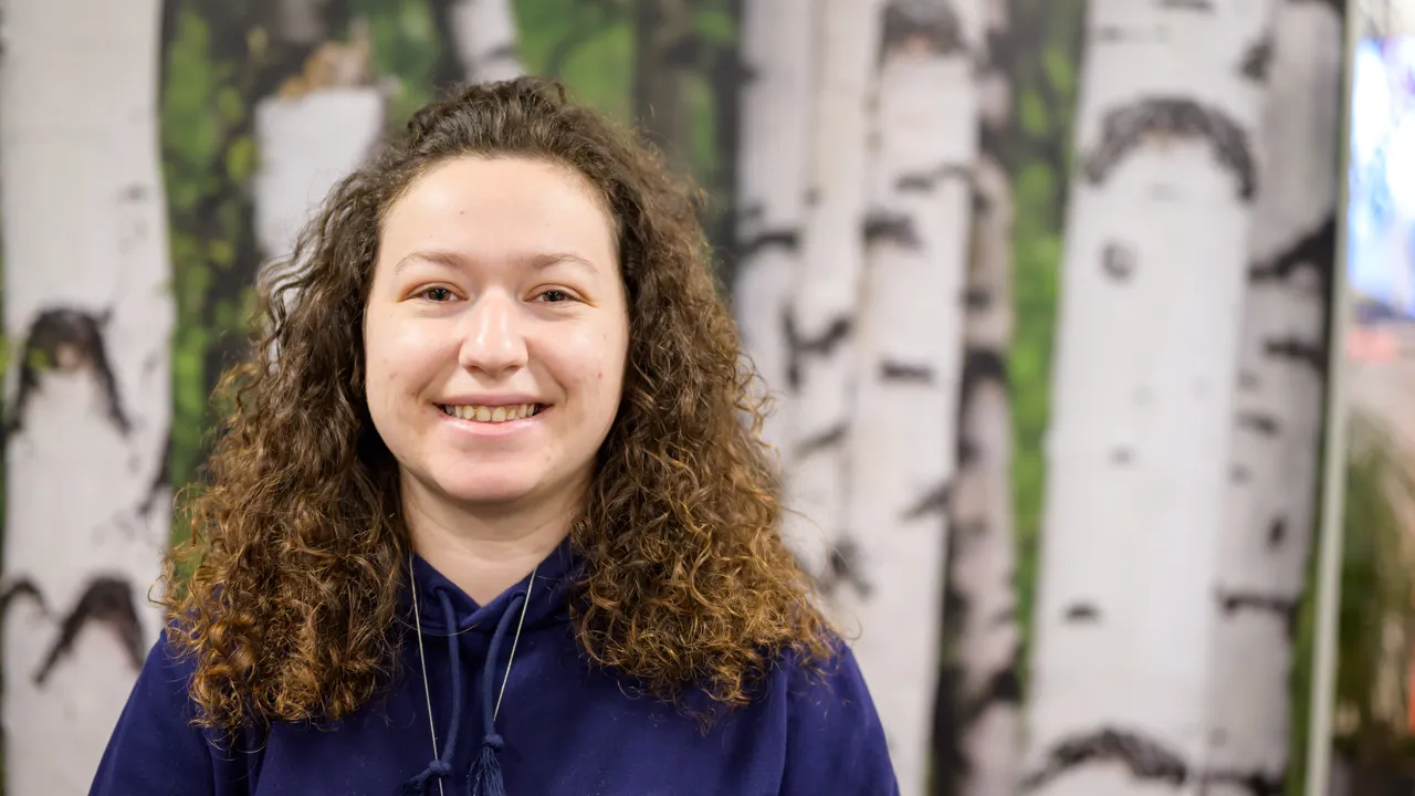 A woman standing in front of a painting of birch trees