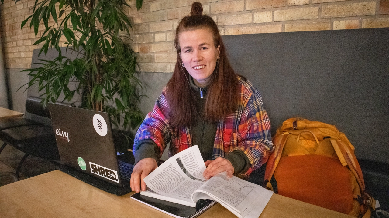 Bild på Sara Andersson sittande vid bord med kursbok och dator framför sig