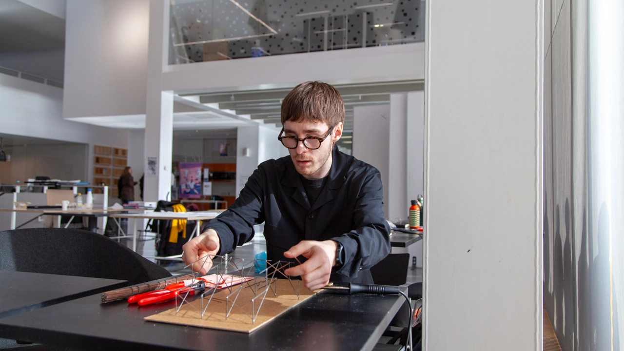 Bild på Simon From sittande vid bord, håller i en arkitektonisk modell i metall