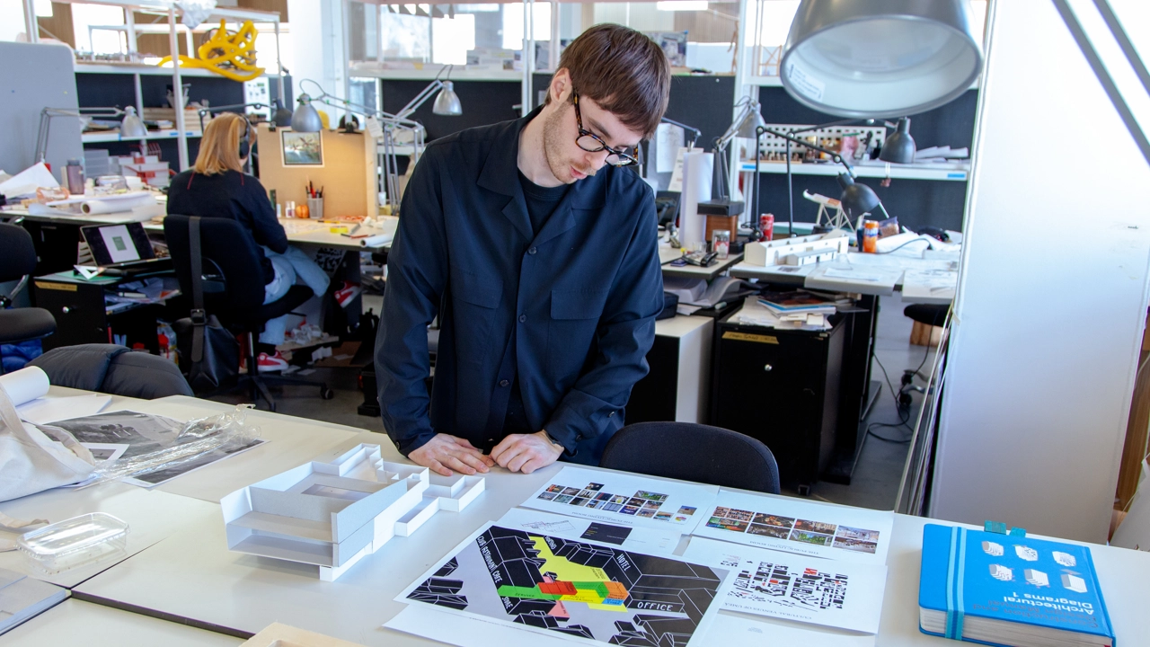 Bild på Simon From stående vid sin studentarbetsplats på Arkitekthögskolan