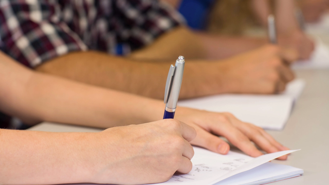 Detalj på händer som skriver på papper. Elever i klassrum.
