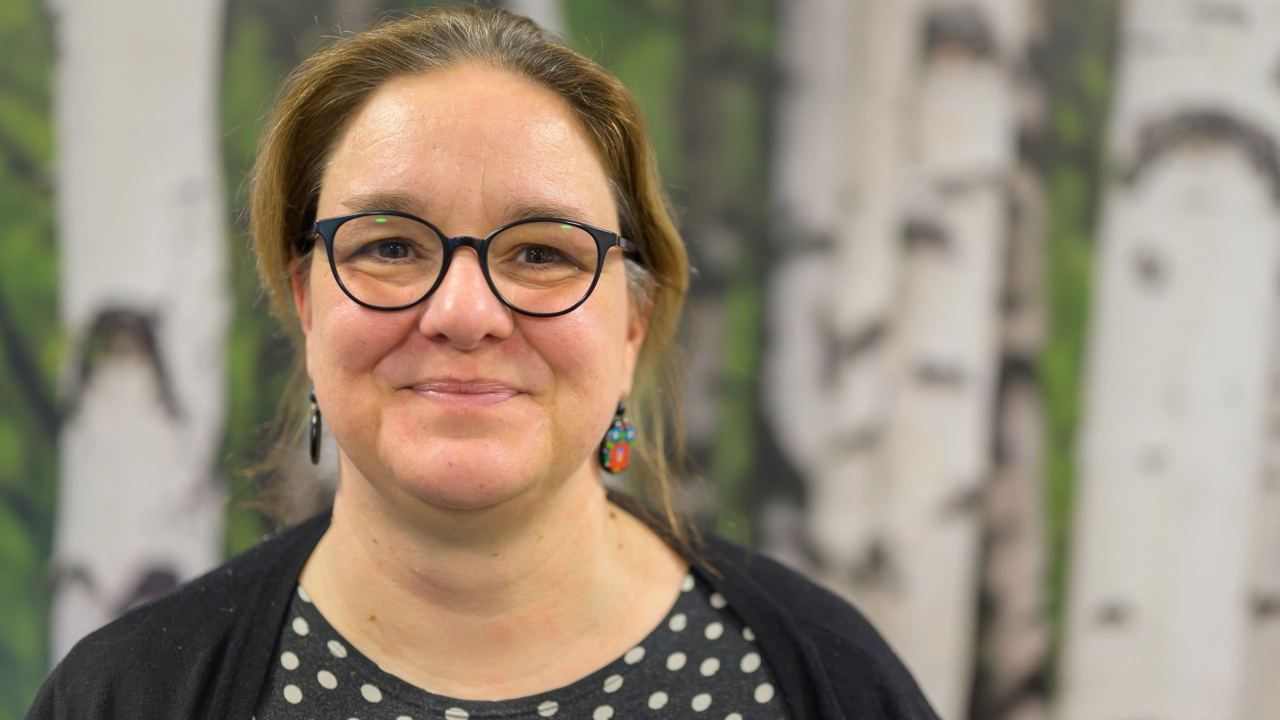 En kvinna med glasögon som står framför en målning av träd