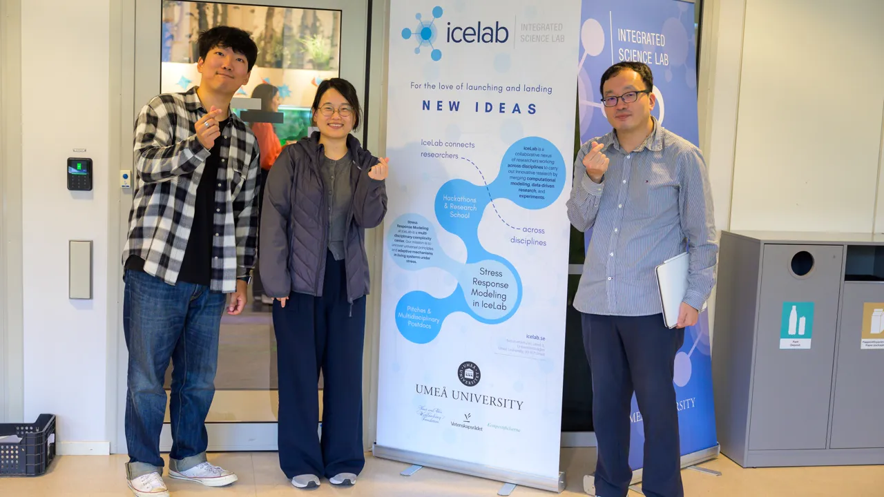 Tre personer står och håller ihop sina fingrar runt en banderoll med reklam för IceLab