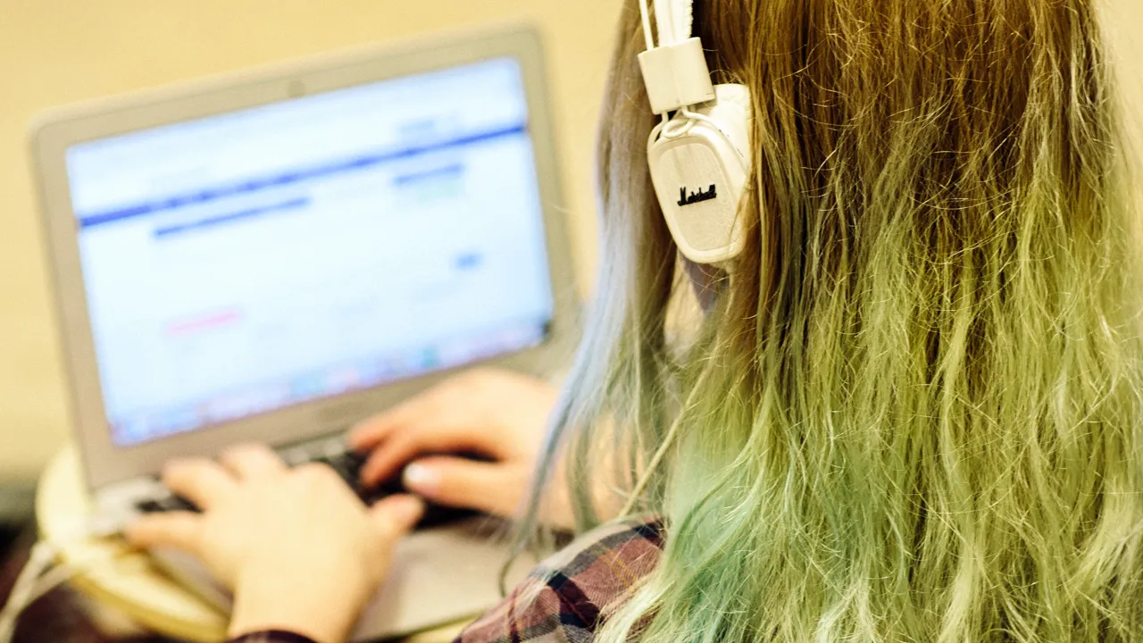 Detalj av student med hörlurar och som skriver på en dator.